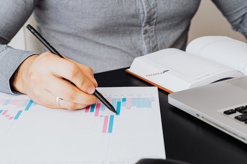 A business analyst examines a graph on paper with a laptop and notebook indoors.