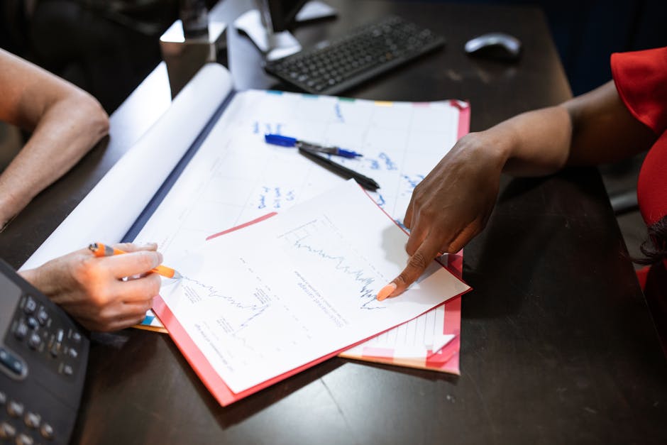 Two people discussing graphs and data on a desk, pointing and writing notes.