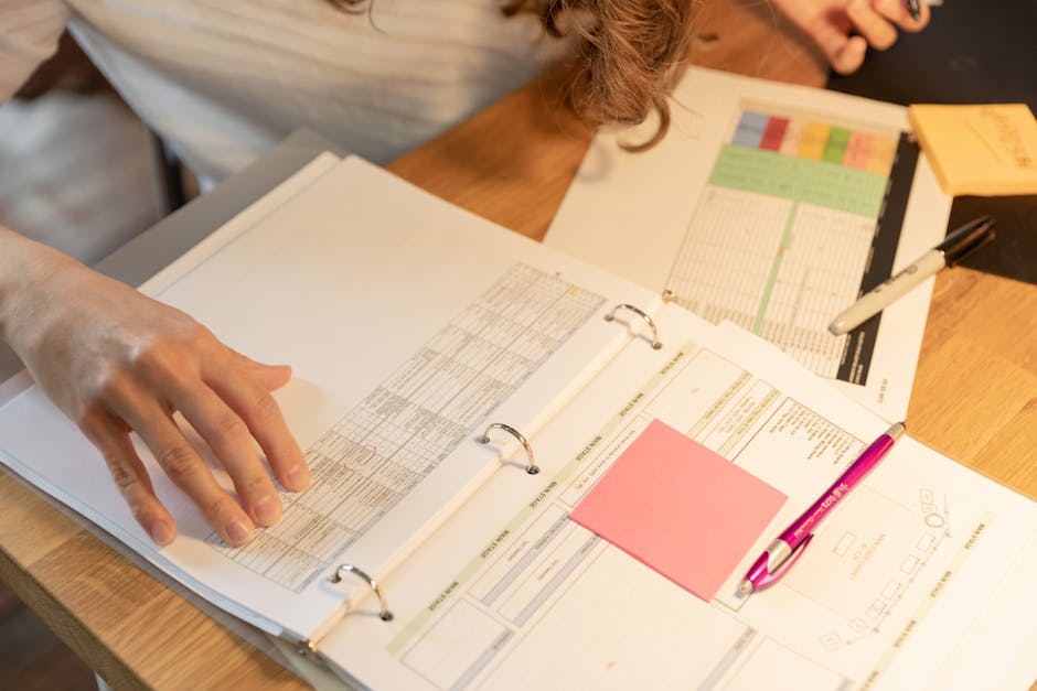 Close-up of an employee sorting documents with sticky notes and pens on a wooden desk.